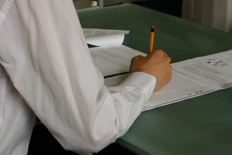 Close-up of a test taker filling in an answer sheet with a pencil at a classroom desk